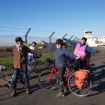 Quelques cyclistes mimant un avion avec les bras tendus devant l'aérodrome de Toussus le Noble