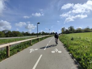 Cycliste de dos, avec un casque, sur une piste cyclable le long d'une route départementale hors agglomération, par beau temps
