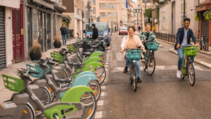 Trois utilisateur·ices de Vélib arrivent à l'approche d'une station dans une petite rue parisienne