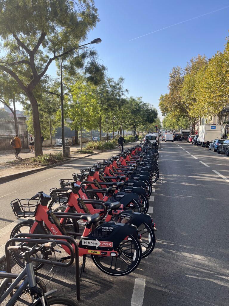 Plusieurs dizaines de vélos en libre service de la marque Voi sur un ensemble d'arceaux