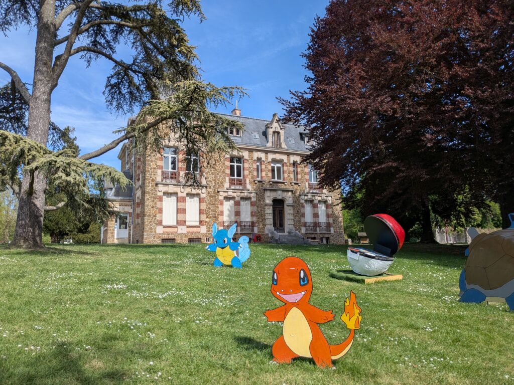 Château du Val des Dames à Gretz-Armainvilliers. Le bâtiment est encadré de deux arbres majestueux. Au premier plan, des Pokémons disposés dans l'herbe.