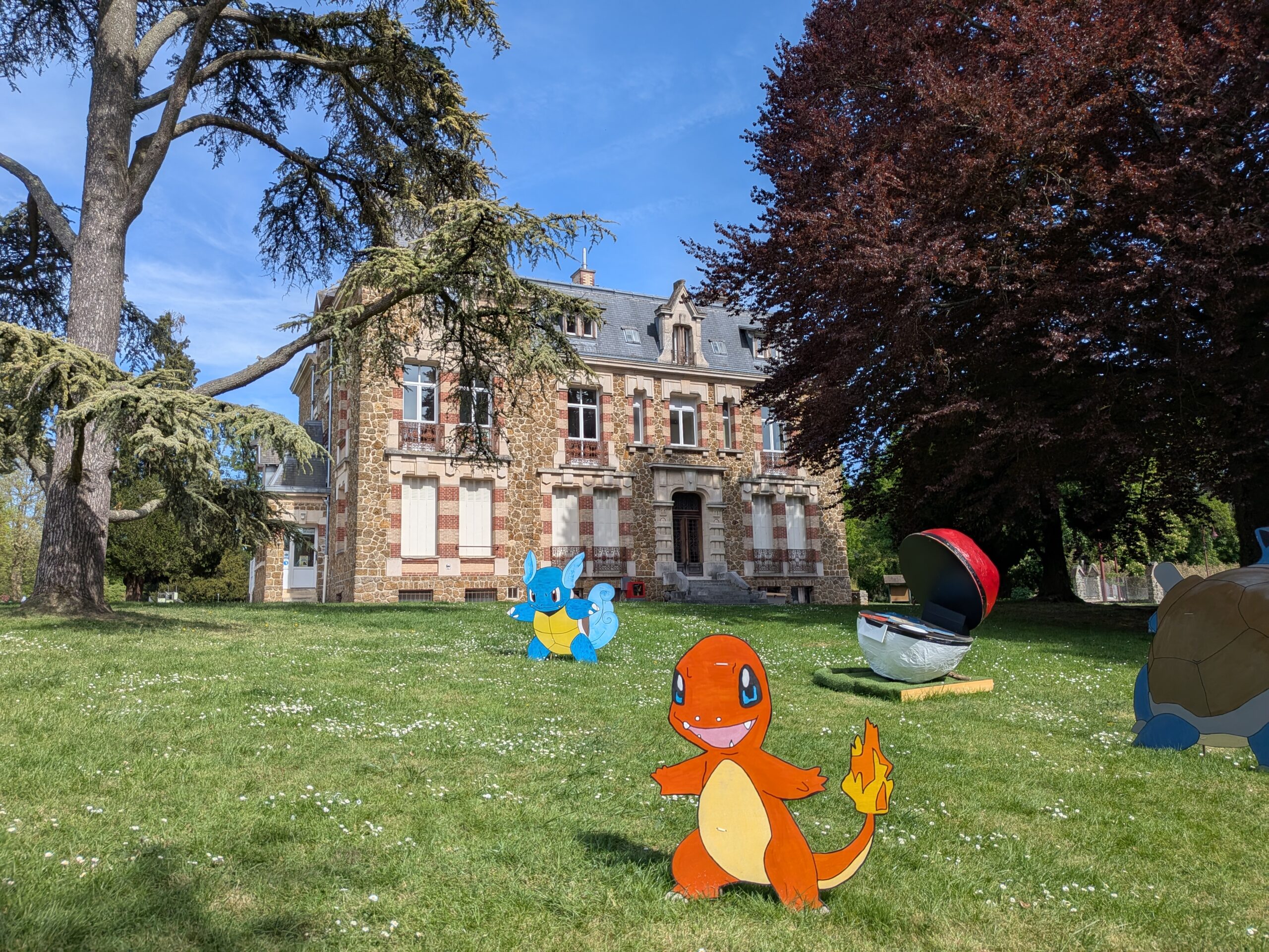 Château du Val des Dames à Gretz-Armainvilliers. Le bâtiment est encadré de deux arbres majestueux. Au premier plan, des Pokémons disposés dans l'herbe.